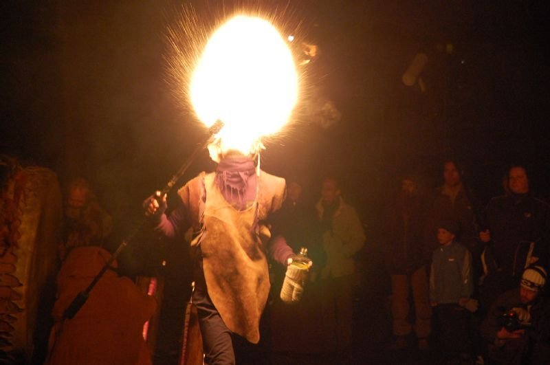 A performer carrying a large blazing torch through a crowd at night.