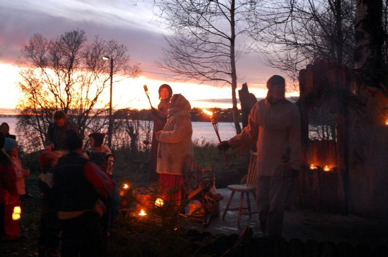 People with torches and lanterns on a lakeshore at dusk.