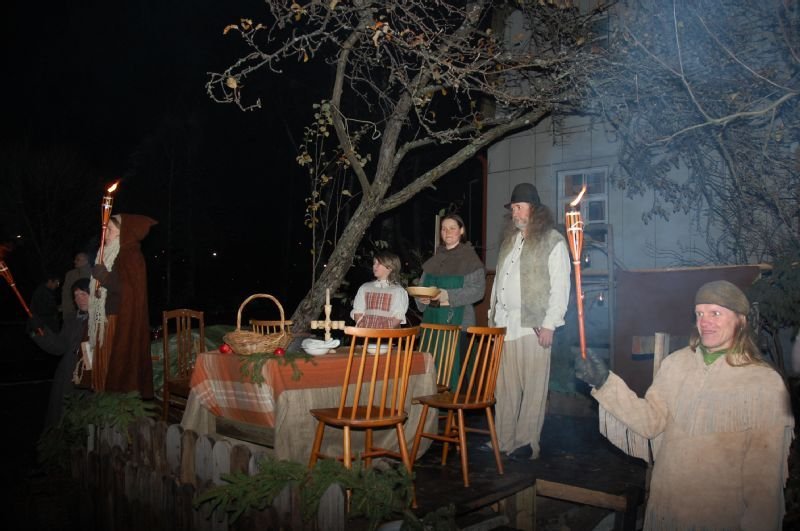 People in long robes with torches beside an outdoor table set for a meal at night.