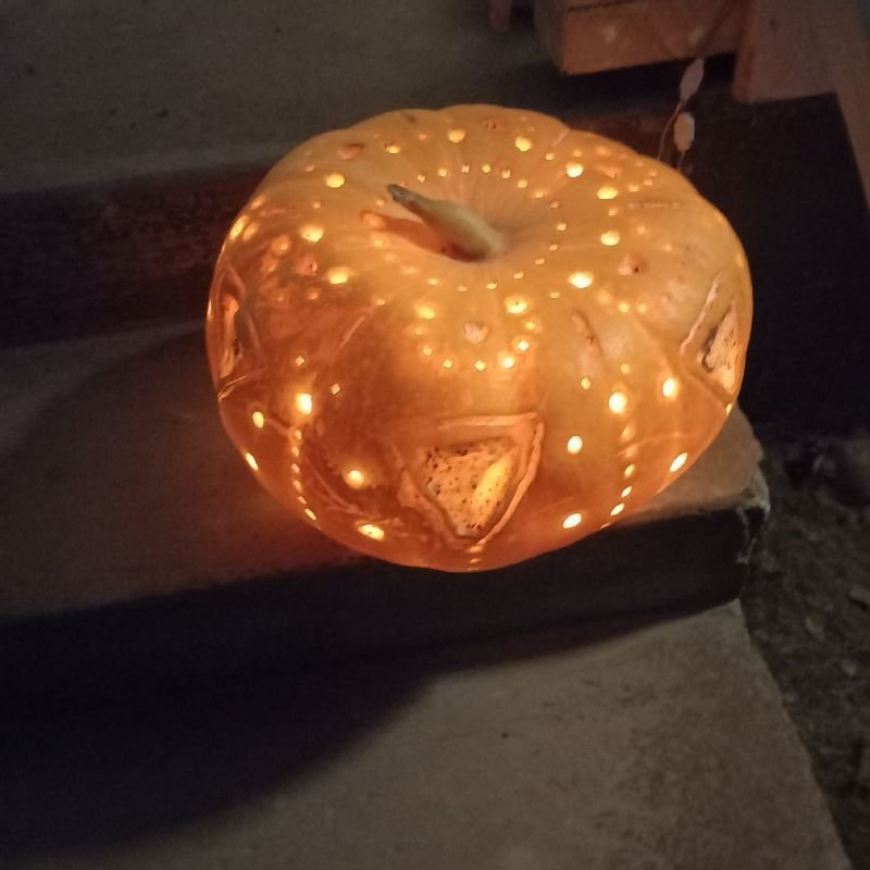 A pumpkin carved with small holes, glowing from a candle inside.