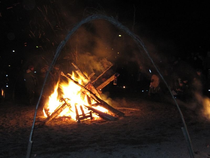 A large bonfire burning at night under a metal arch.
